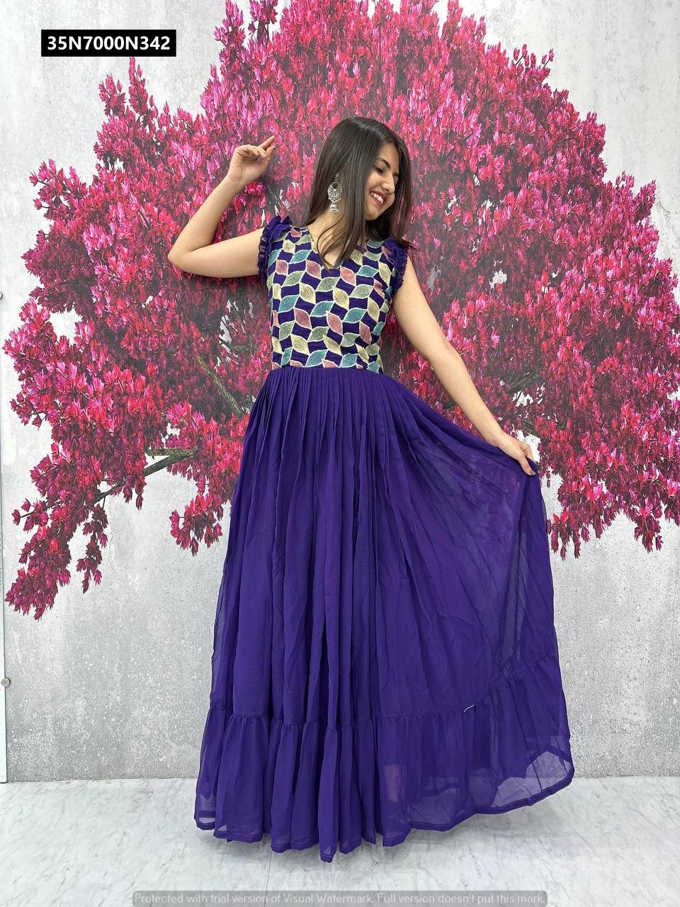 Model in a deep purple TRENDBUY Fox Georgette gown, smiling and posing against a pink floral background, showcasing the full flair and elegant fall of the fabric.
