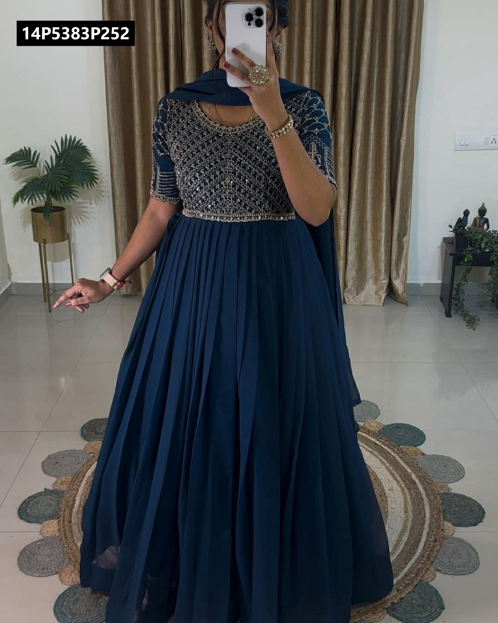 Model wearing a blue TRENDBUY georgette gown with intricate embroidery and a matching dupatta, standing in a contemporary living space.