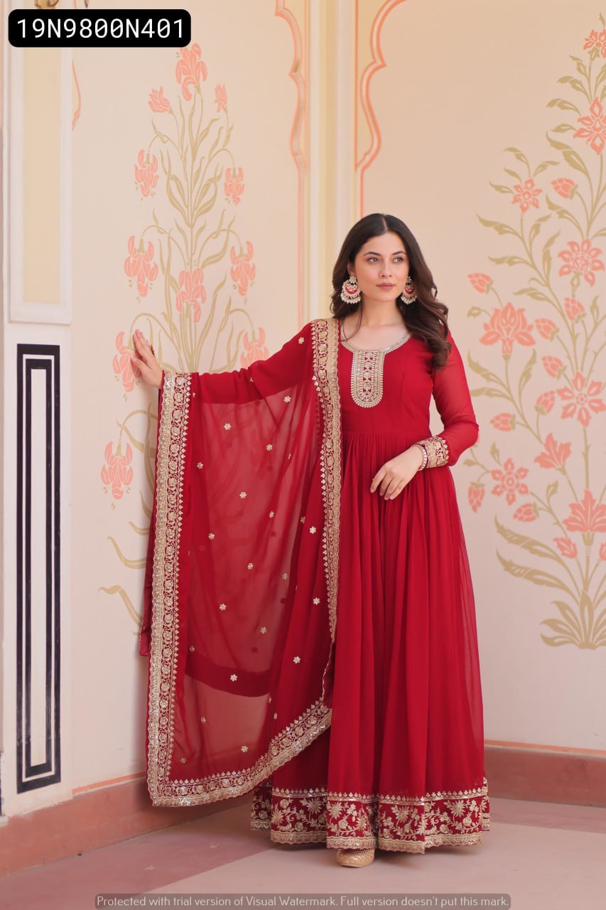 Model posing elegantly in a TRENDBUY Maroon Embroidered Georgette Gown with Dupatta, standing by a traditional patterned wall.