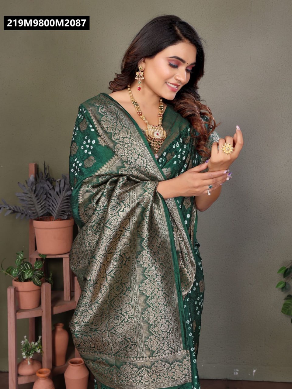Model smiling, adjusting the pallu of an emerald green Bandhej satin silk saree with gold zari weaving.