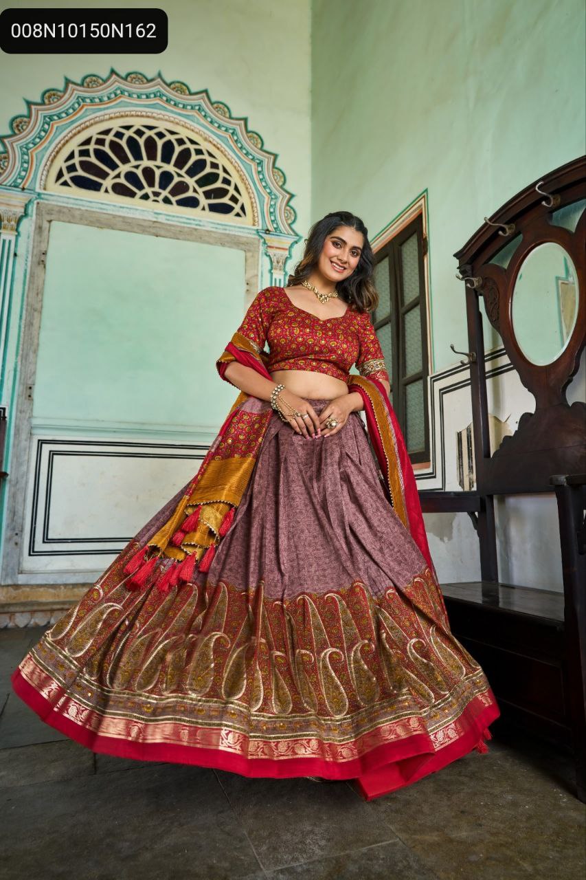 TRENDBUY model gracefully posing in a maroon and mauve Tussar Silk Lehenga Choli with gold Kashmiri and foil print, showcasing its full flair and tassels, set against a traditional archway.