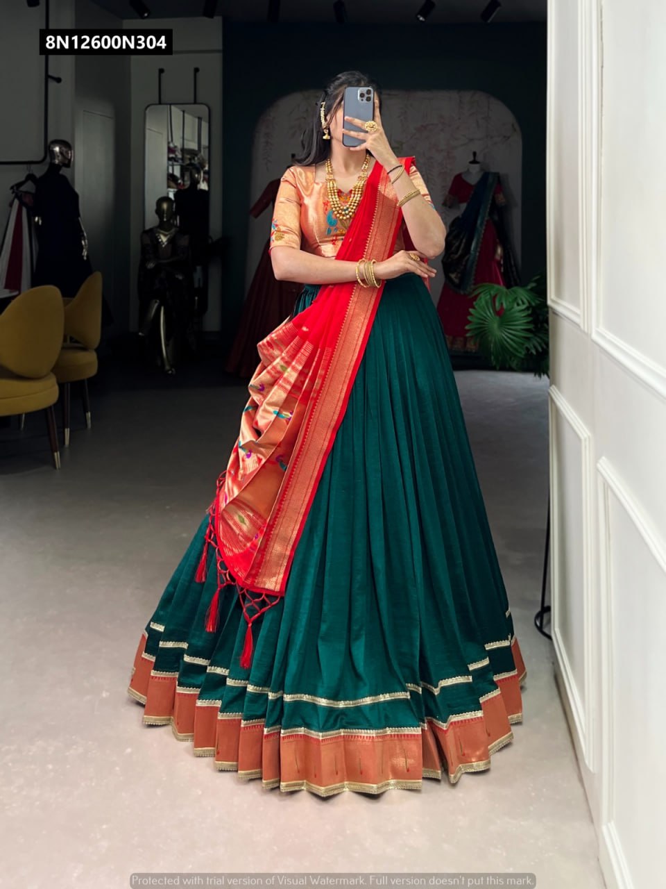 Full body shot of model wearing a deep teal Vichitra silk lehenga with a red zari weaving dupatta and peach Jacquard blouse, showcasing the ensemble's intricate work and flare.
