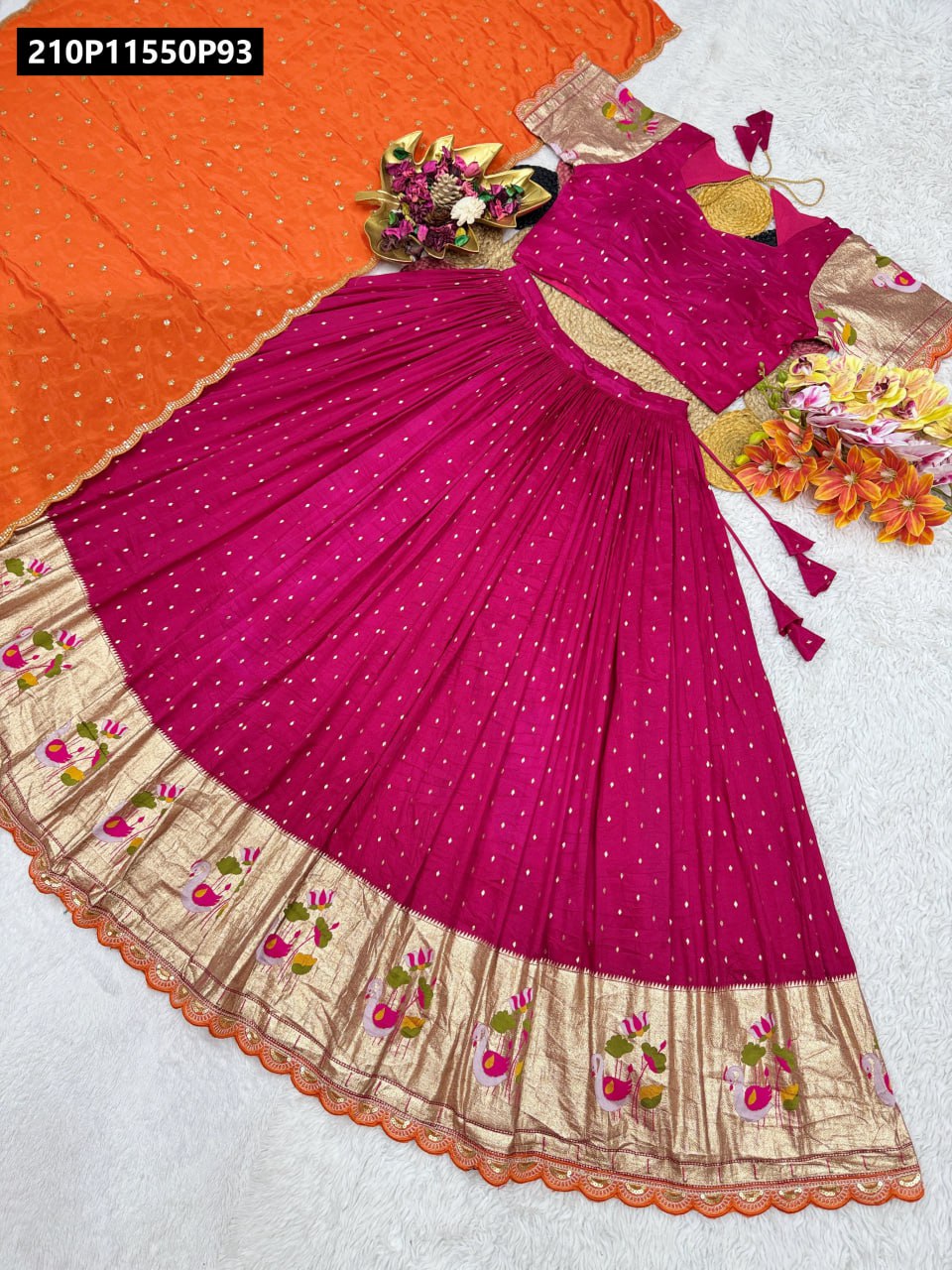 TRENDBUY Pink Viscose Dola Silk Lehenga Choli set with gold sequins, featuring a traditional border and an orange chinnon dupatta, artfully arranged on a white background.