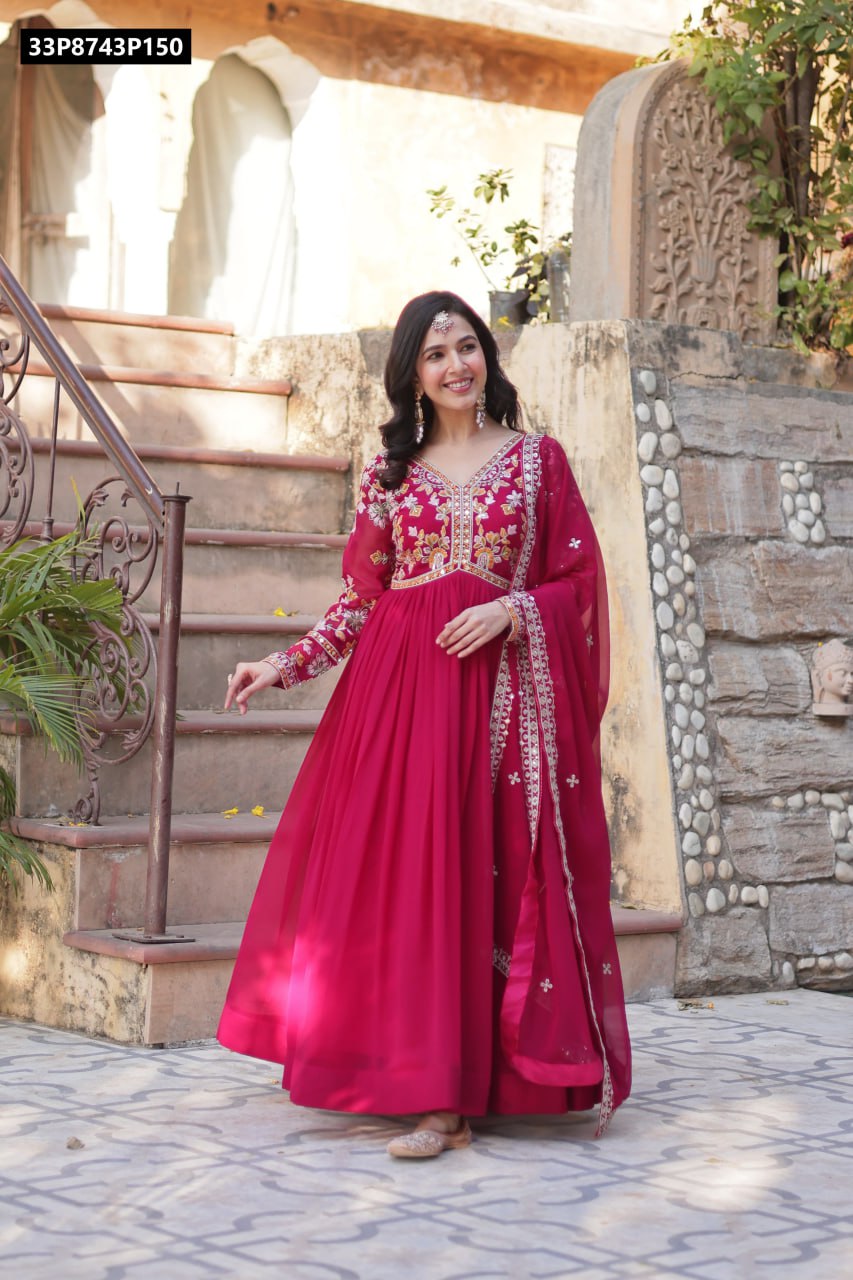 A model elegantly standing on ancient stone steps, showcasing a full-length magenta Faux Blooming Anarkali gown with intricate sequins embroidery.