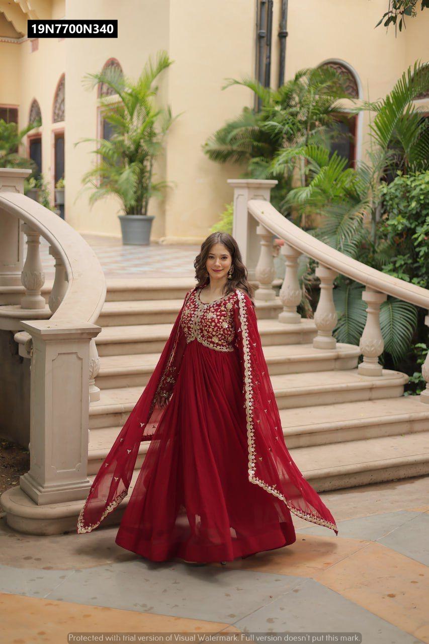 TRENDBUY model gracefully standing in a full-length maroon embroidered gown with flowing dupatta on outdoor stairs.