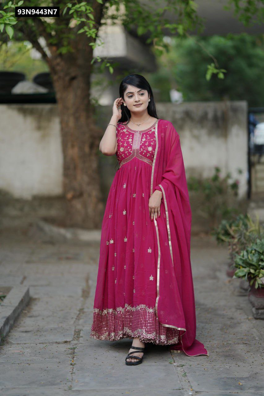 Full shot of a model elegantly posing in a sleeveless pink faux georgette Aliya cut gown, adorned with gold embroidery and sequin work, paired with a matching dupatta, outdoors amidst greenery.