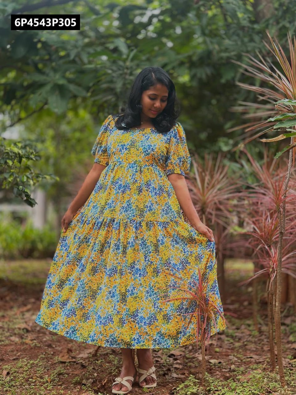 Model in yellow, blue, and green floral Fox Georgette tiered midi dress, posing happily in a lush garden setting.