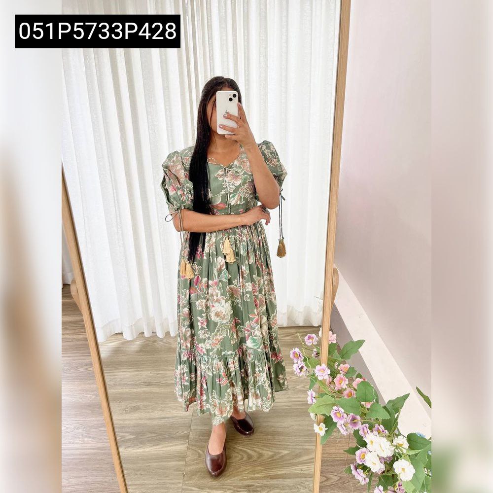 Model wearing the Pishta green floral Roman silk gown, standing poised in a mirror, displaying the full elegant silhouette and floral pattern.