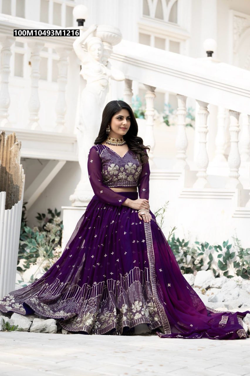 TRENDBUY purple georgette lehenga choli with heavy gold sequin embroidery, modeled gracefully by a woman against a white architectural background.