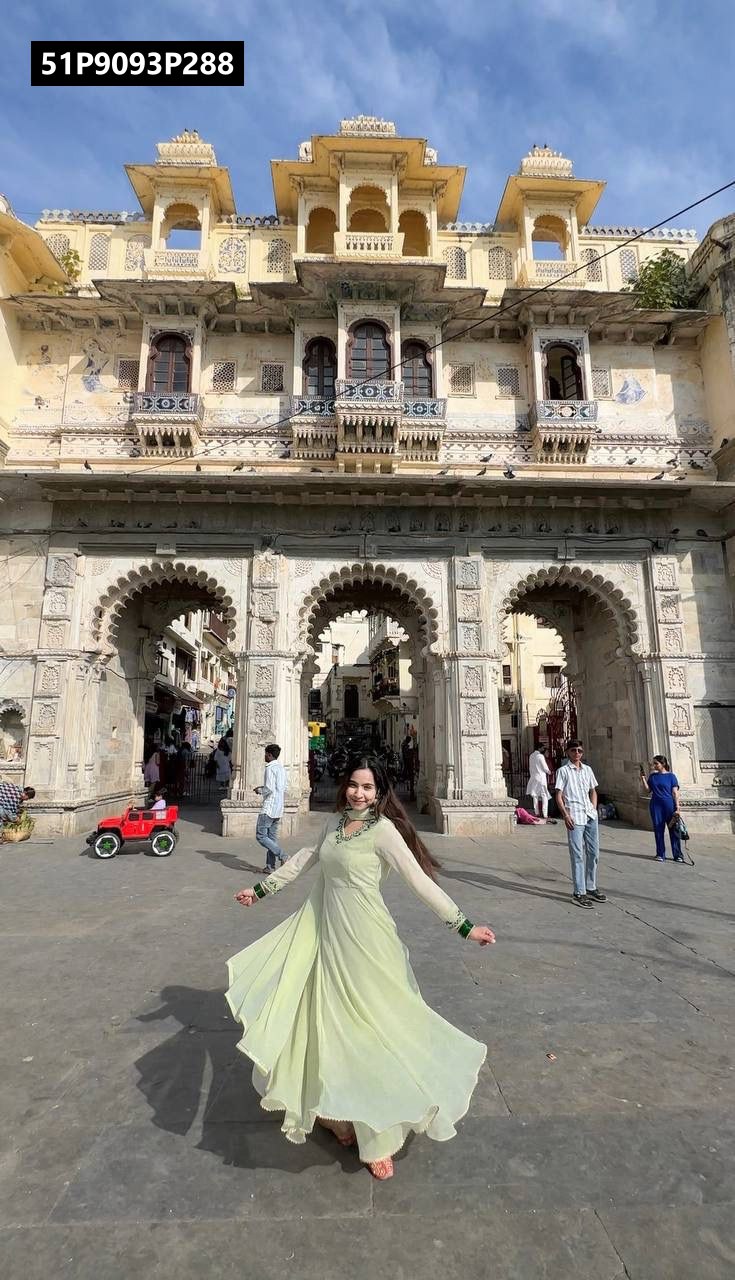 Model twirling in a pistachio green TRENDBUY Fox Georgette Anarkali gown with handwork embroidery, standing in front of an ancient Indian palace.