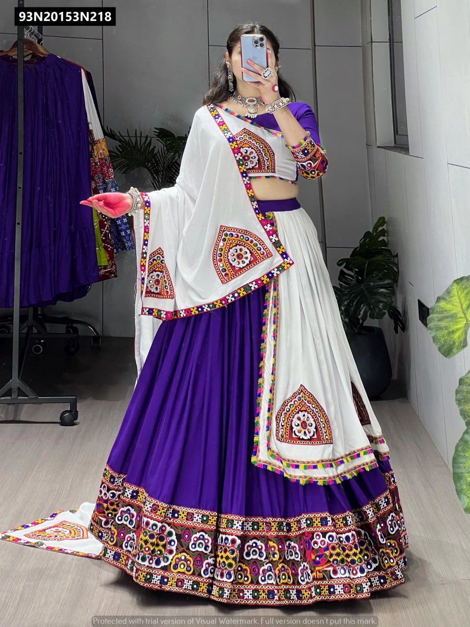 Full body shot of a model elegantly posing in a purple TRENDBUY Gamthi mirror work lehenga choli set with a white embroidered overlay dupatta, showcasing a 6-meter flair.