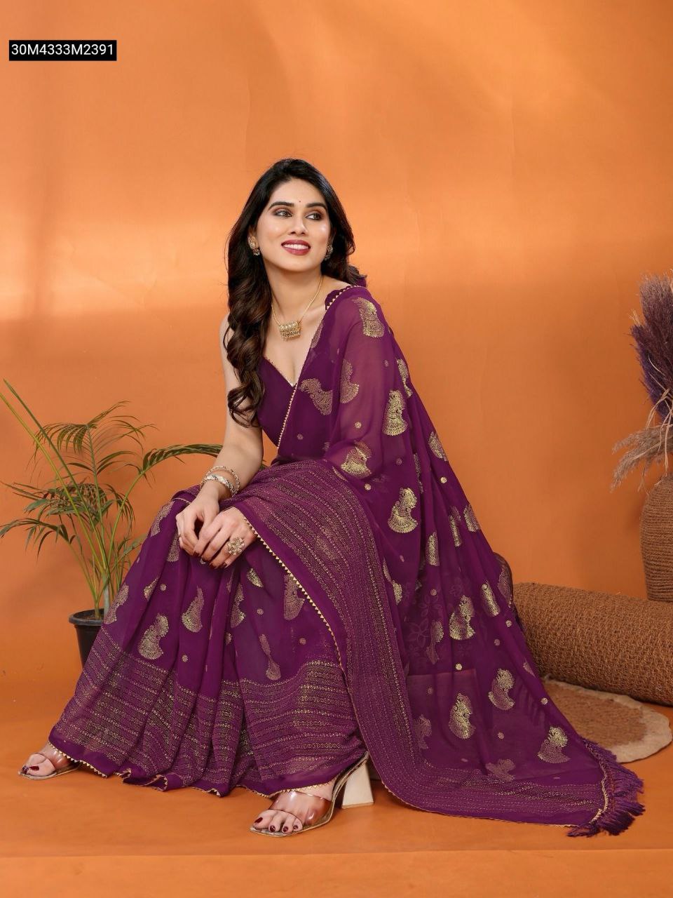 TRENDBUY Plum Purple Georgette Silk Saree with gold paisley foil work and lace border, draped elegantly on a model sitting against an orange background.