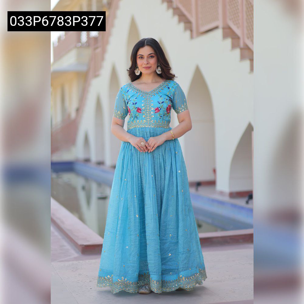 Full body shot of a model wearing a light blue TRENDBUY Gold Crush embroidered V-neck gown, standing gracefully in an outdoor setting by a pool.