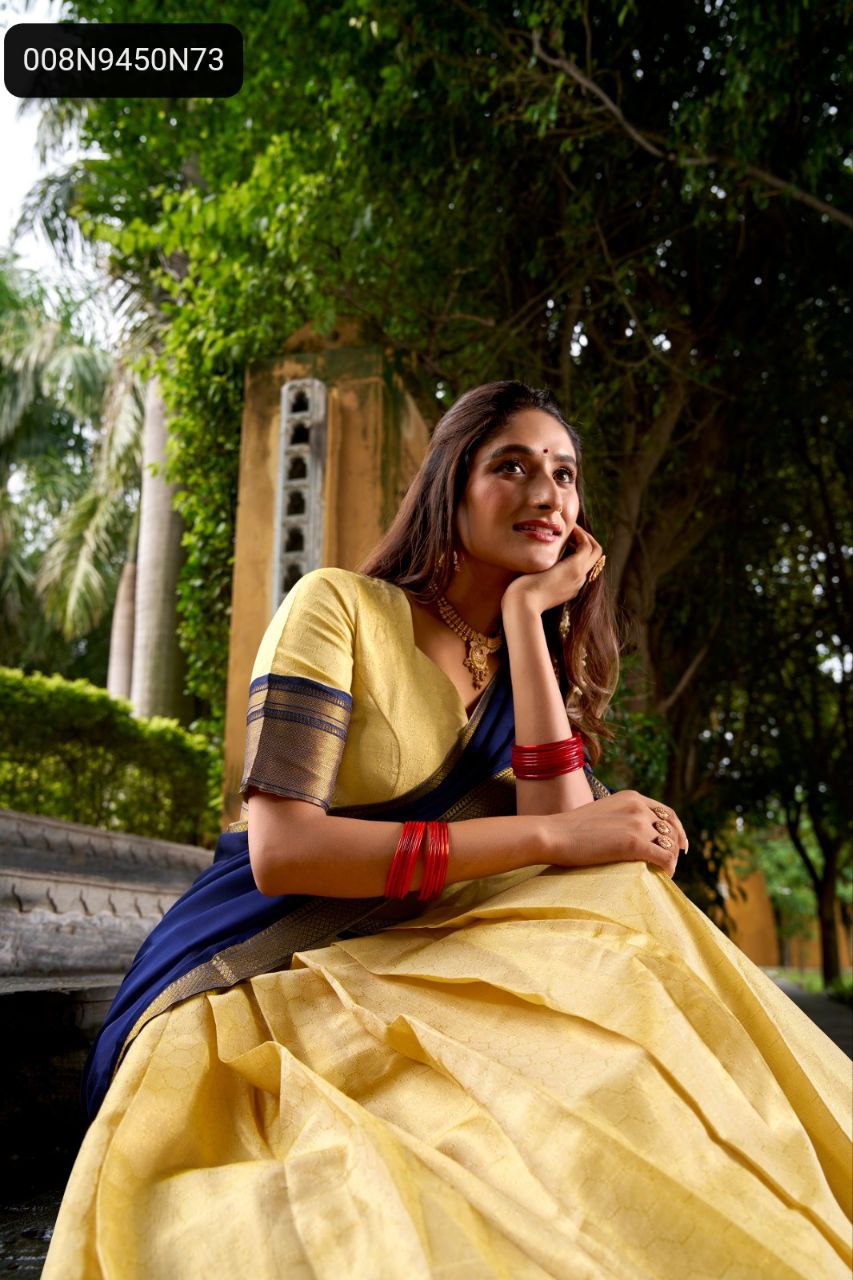 A model in a TRENDBUY golden Kanchipuram lehenga and navy blue dupatta, seated on outdoor steps, looking thoughtful with subtle traditional accessories.