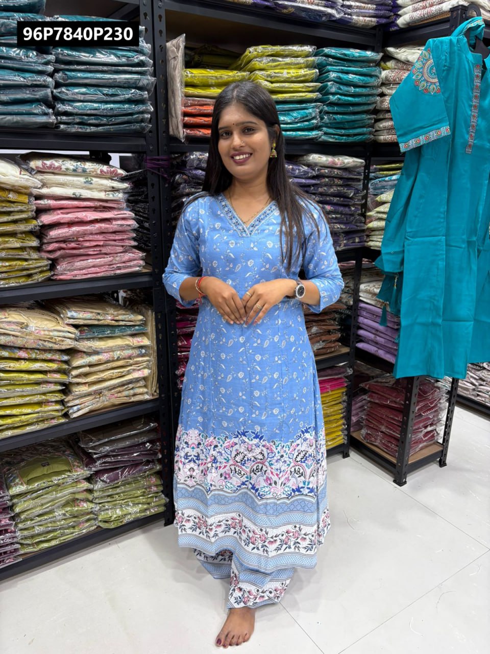 Full body shot of a woman modeling the TRENDBUY light blue floral print cotton kurti set with V-neck hand work, standing in a store.