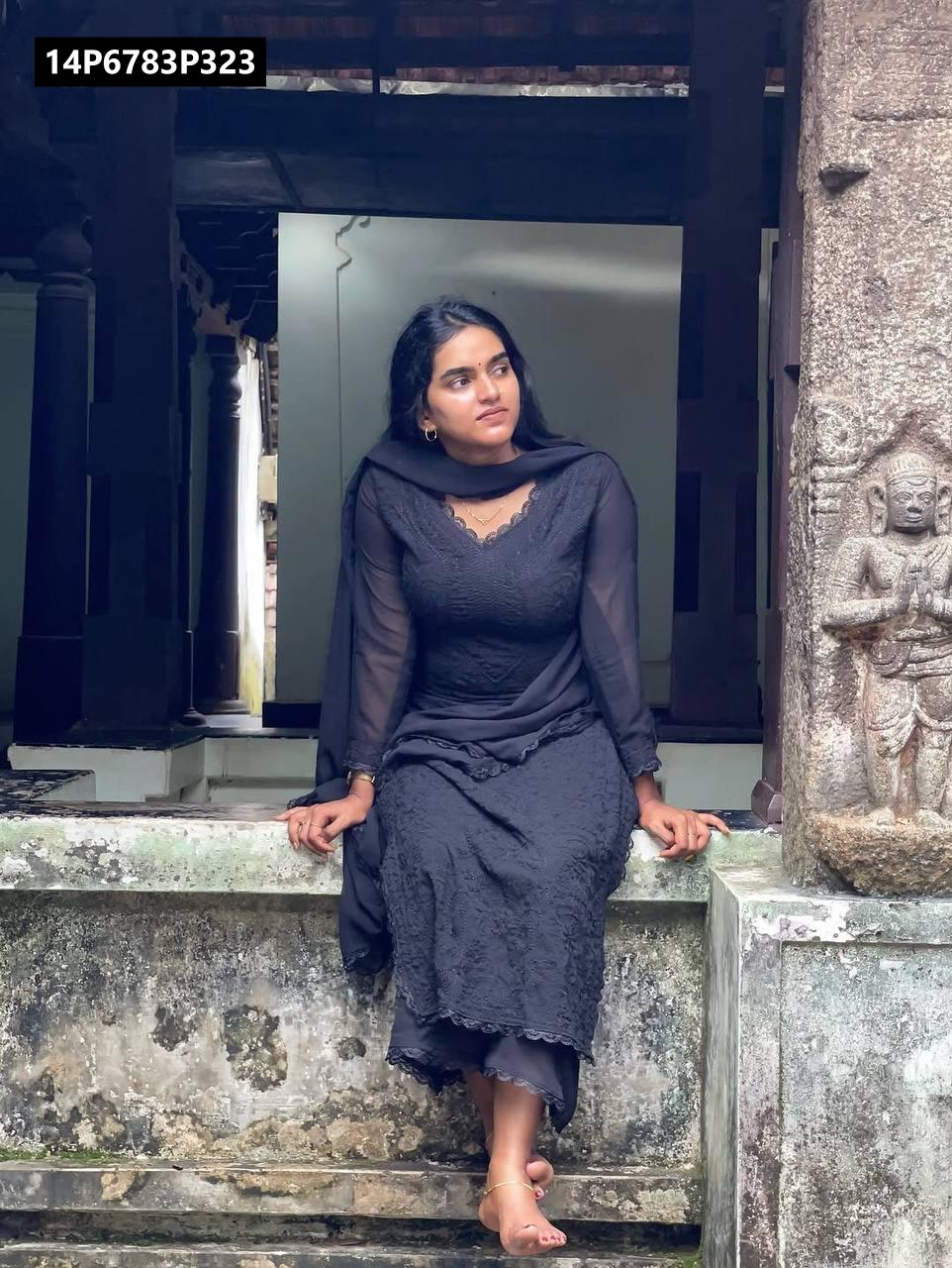 Model in black heavy faux georgette embroidered kurti set, seated on a traditional stone ledge, looking thoughtful.