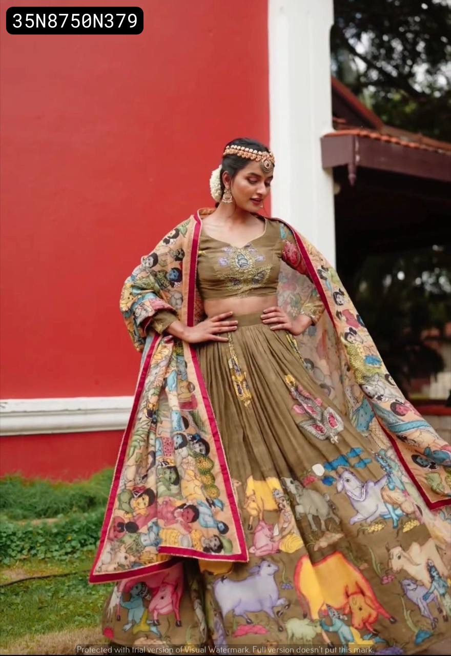 Full-body shot of a smiling model in an olive green Kalamkari print lehenga choli set, showcasing the wide flair of the lehenga and the flowing dupatta against a red wall.