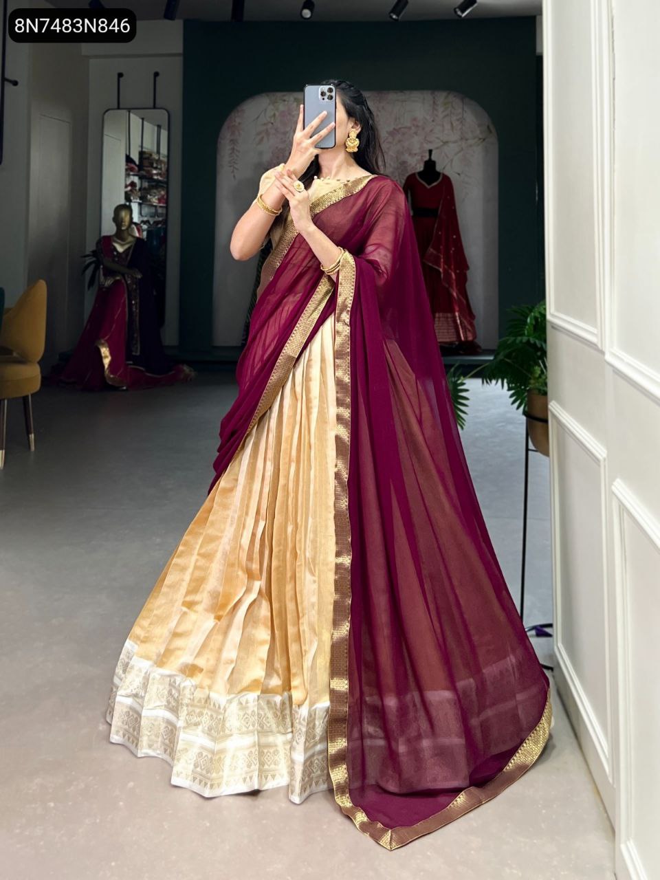 Model in TRENDBUY Gold Kanchipuram lehenga with Maroon Zari weaving blouse and dupatta, holding phone in a boutique setting.