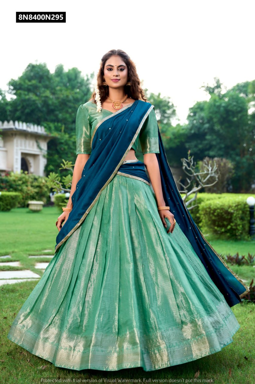 Main product image: Full-length shot of model showcasing the detailed green Kanchipuram zari weaving lehenga and teal silk dupatta with embroidery, captured in a scenic garden.