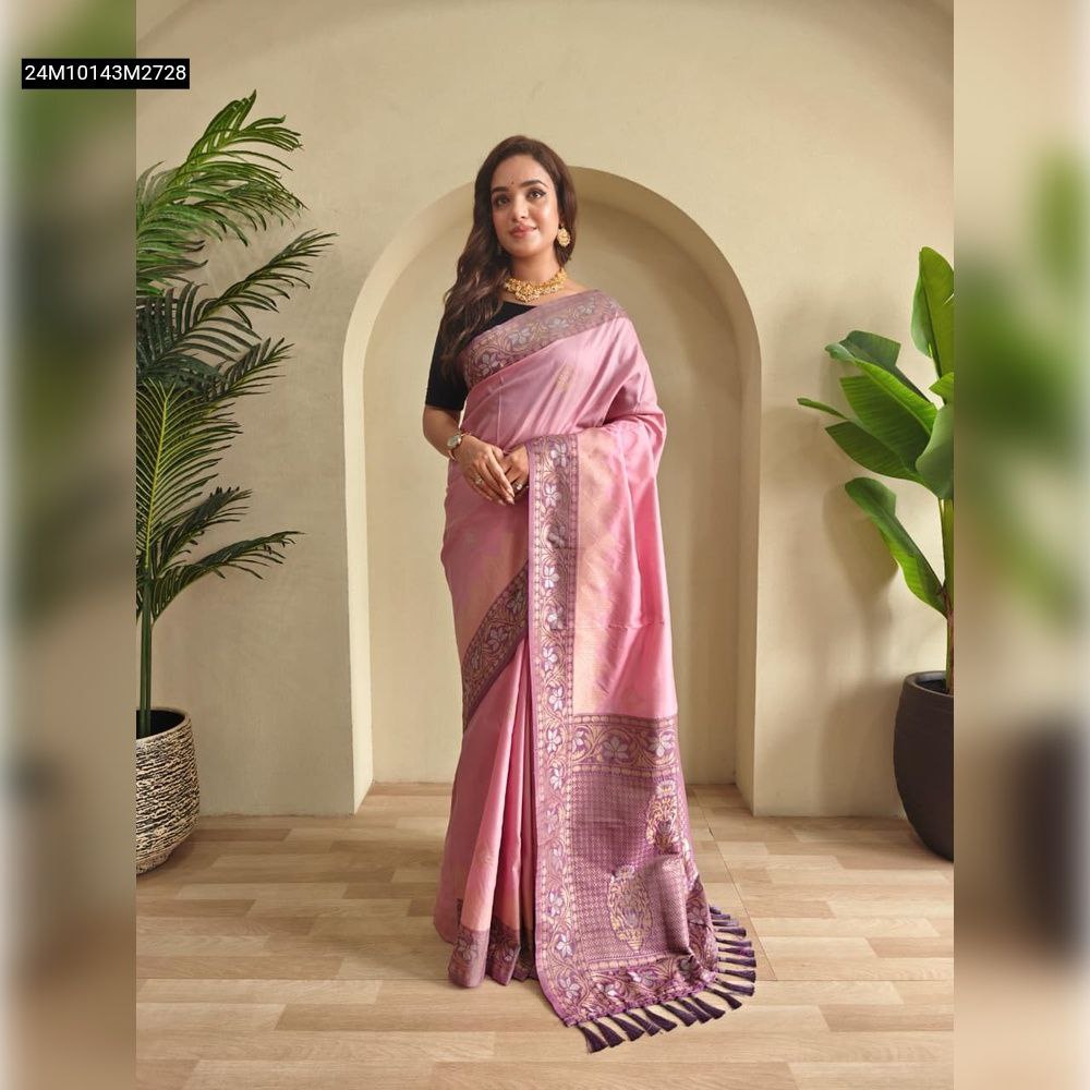 Full length shot of a woman modeling a light pink dual-tone silk saree with intricate zari weaves and a contrasting purple-pink pallu with tassels, standing against an arched wall.