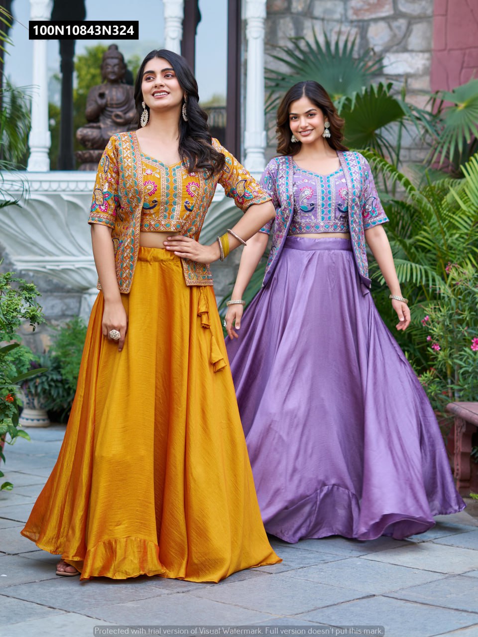 Two models showcasing TRENDBUY pure Vichitra lehenga choli sets with embroidered kotis, one in mustard gold and one in lavender purple, in an outdoor setting.