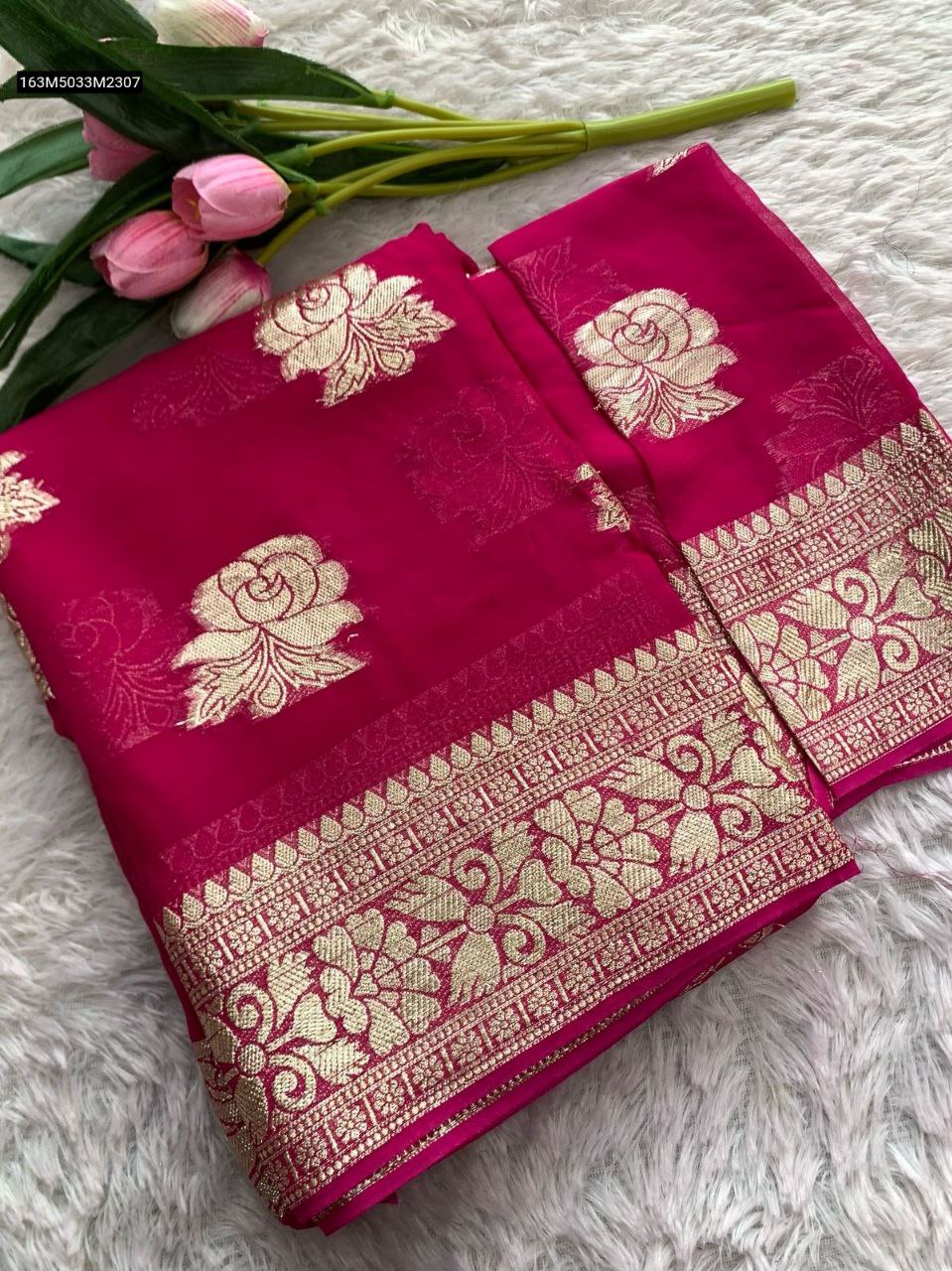 TRENDBUY Hot Pink Viscose Georgette Saree with intricate gold zari floral weaving on pallu and border, folded neatly on a white textured surface with pink tulips.