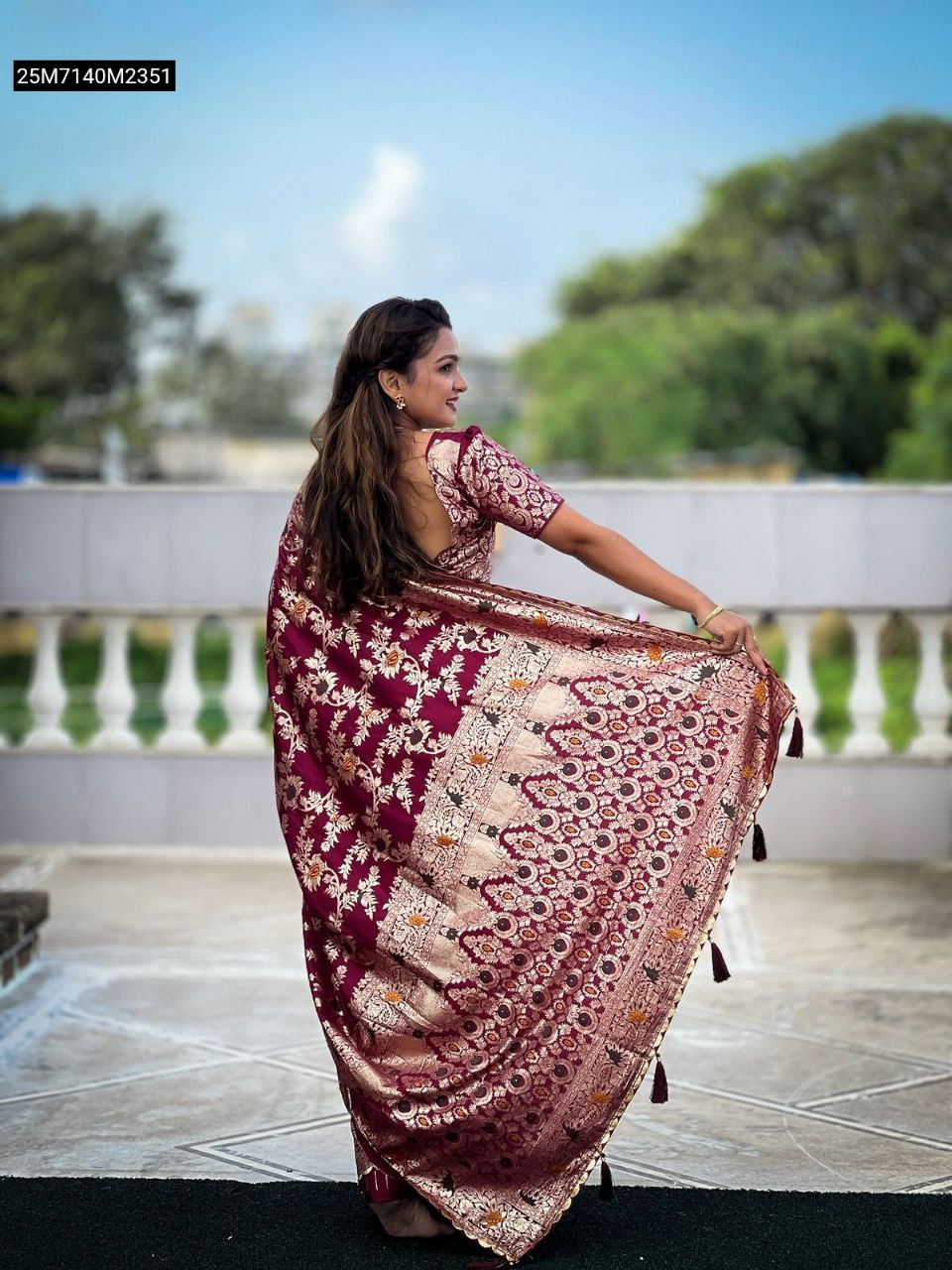 Model from behind showcasing the TRENDBUY Maroon Dolla Silk Saree's rich Meenakari pallu and tassels against a natural backdrop.