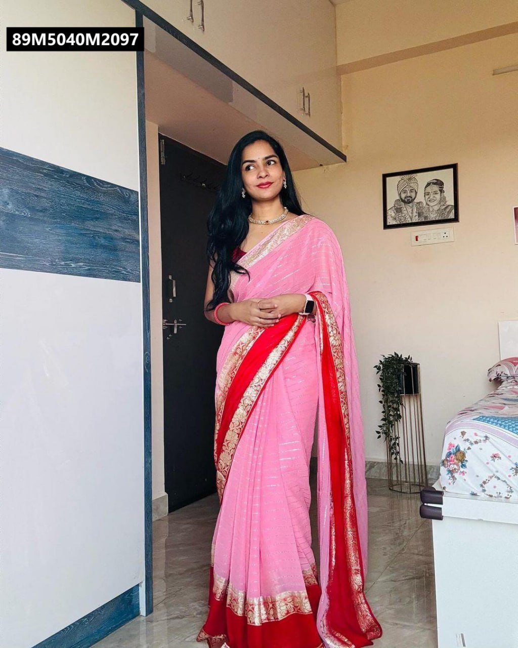 Model wearing a TRENDBUY Pink Viscose Georgette saree with gold zari stripes and red floral border, standing in a room.