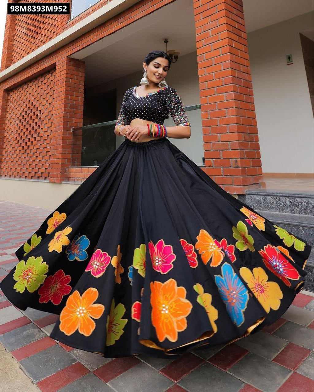 Model in a dynamic pose, gracefully twirling the TRENDBUY black Maslin Silk Lehenga, emphasizing the magnificent flair and the colorful floral patterns along the lower edge of the skirt.