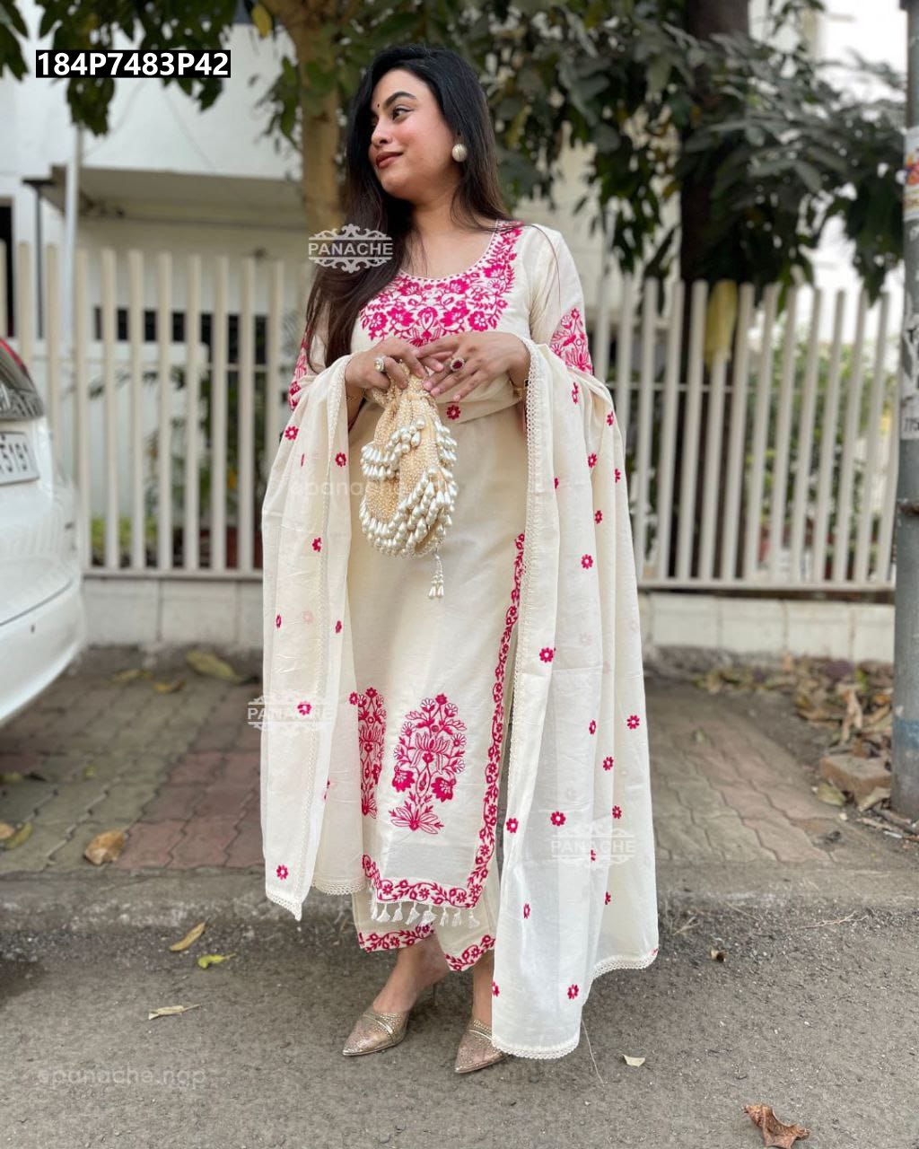 Full body shot of a woman in an elegant off-white Banarasi silk kurti set with intricate pink floral embroidery, holding a pearl-beaded bag.