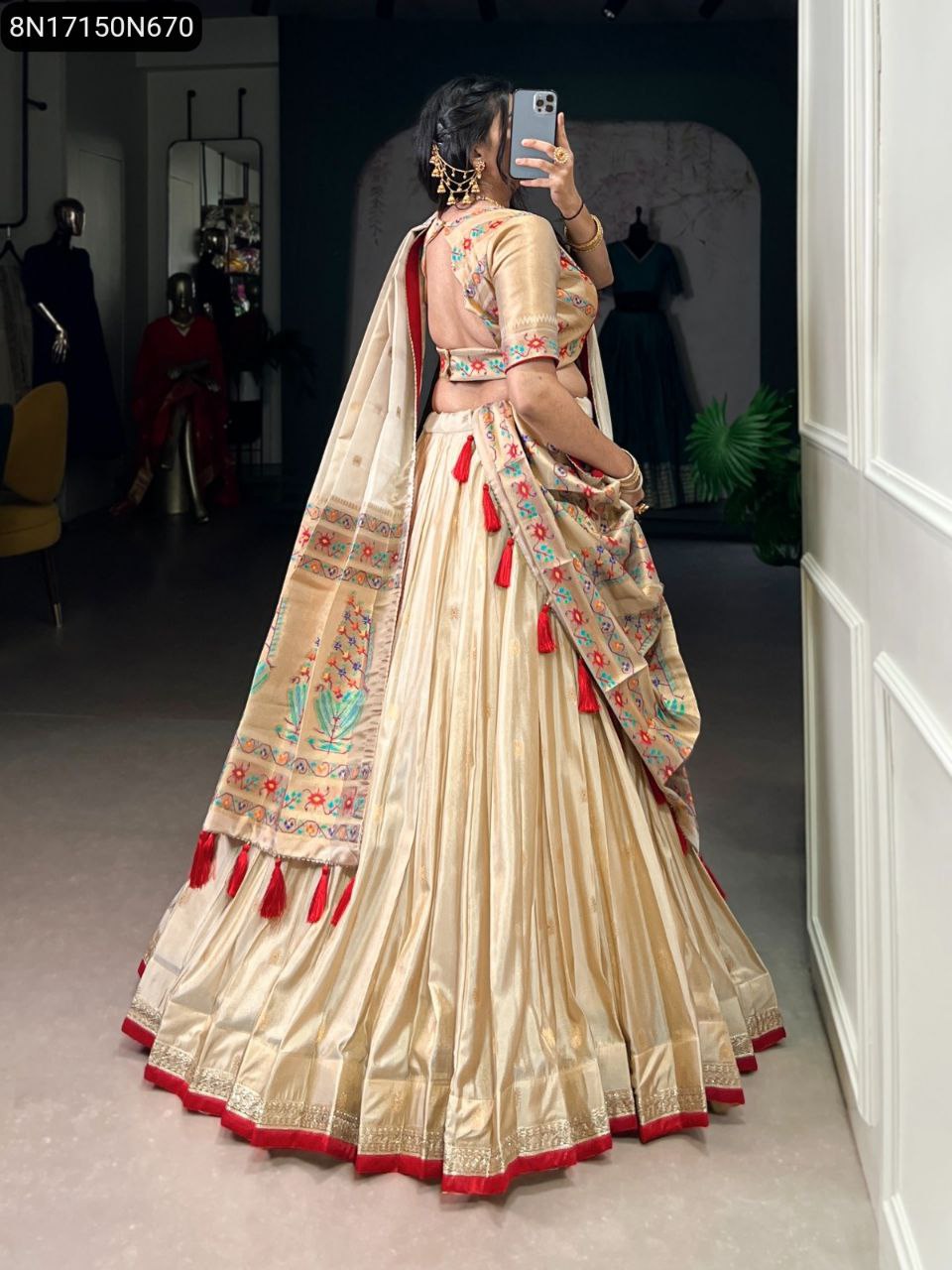 Full-body view of a woman from behind, showcasing a TRENDBUY Paithani-style lehenga choli with a striking red border and matching tassels on the dupatta, standing in an elegant interior.