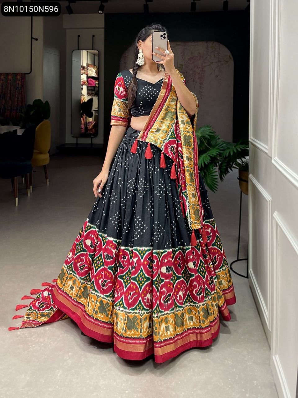 Full body shot of a model wearing a black Tussar silk lehenga choli with vibrant red, green, and gold Patola print border and matching dupatta, showcasing the intricate tassels.