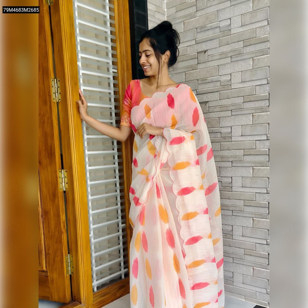 Full shot of a woman wearing a TRENDBUY peach-pink linen saree with vibrant orange and pink digital brushstroke prints, standing by a wooden door with a relaxed smile.