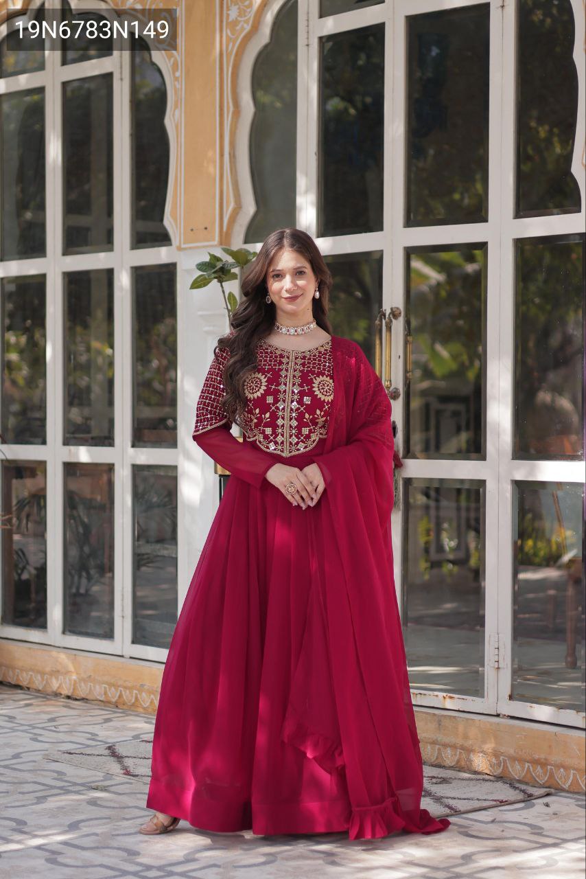 Full body shot of a model elegantly posing in a TRENDBUY magenta embroidered faux georgette gown with dupatta in a decorative outdoor setting.