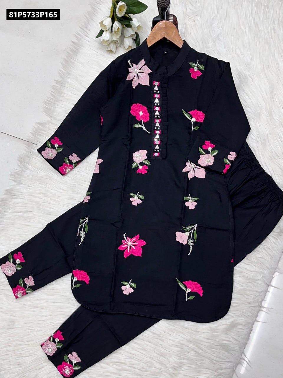Full view of the TRENDBUY black Roman silk kurti and pants set on a wooden hanger, showcasing vibrant pink floral embroidery and original mirror embellishments.