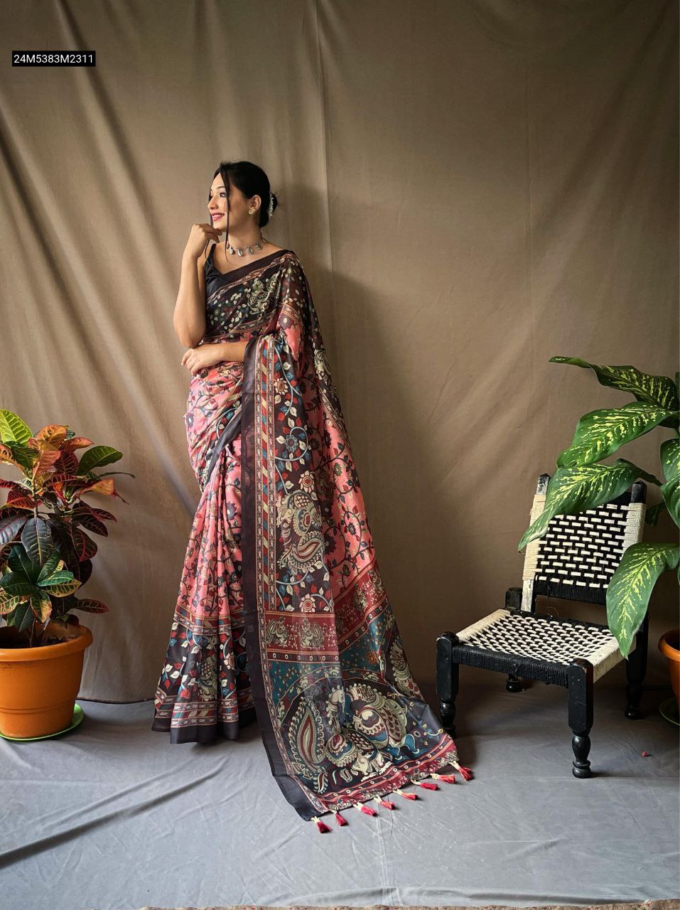 TRENDBUY model in elegant Pink Kalamkari Pure Cotton Saree with contrast pallu and tassels, posing gracefully amidst plants.