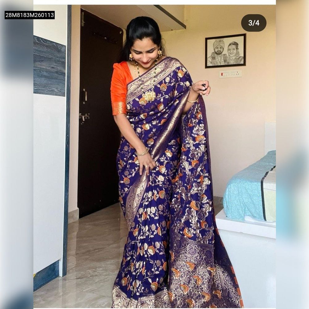 Full shot of a model elegantly draped in a TRENDBUY Royal Blue Khadi Georgette silk saree, showcasing its intricate golden zari and floral Meenakari weaving, perfectly paired with a bright orange contrast blouse, captured indoors.