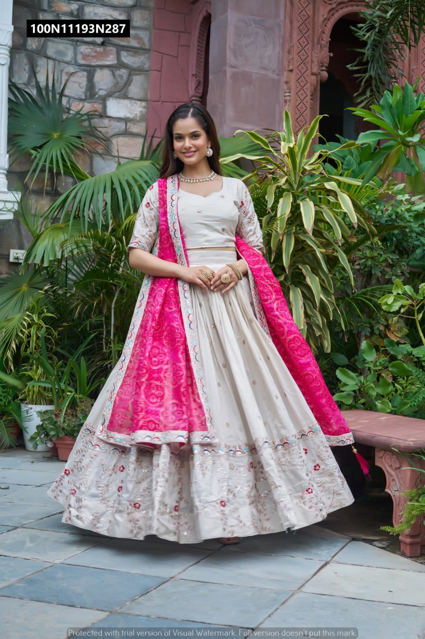 Full-body shot of a model elegantly posing in a TRENDBUY Pure Tissue Silk Lehenga Choli with a vibrant Pink Bandhani Dupatta, standing outdoors and showcasing the skirt's rich embroidery and voluminous flair.