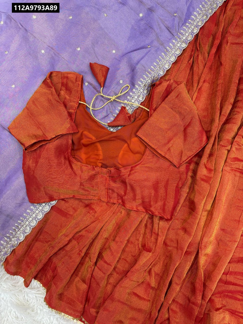 TRENDBUY Rust Orange Viscose Lehenga and Blouse with Lavender Purple Dupatta, featuring gold embroidered border and small embellishments on dupatta, flat lay on white fur.