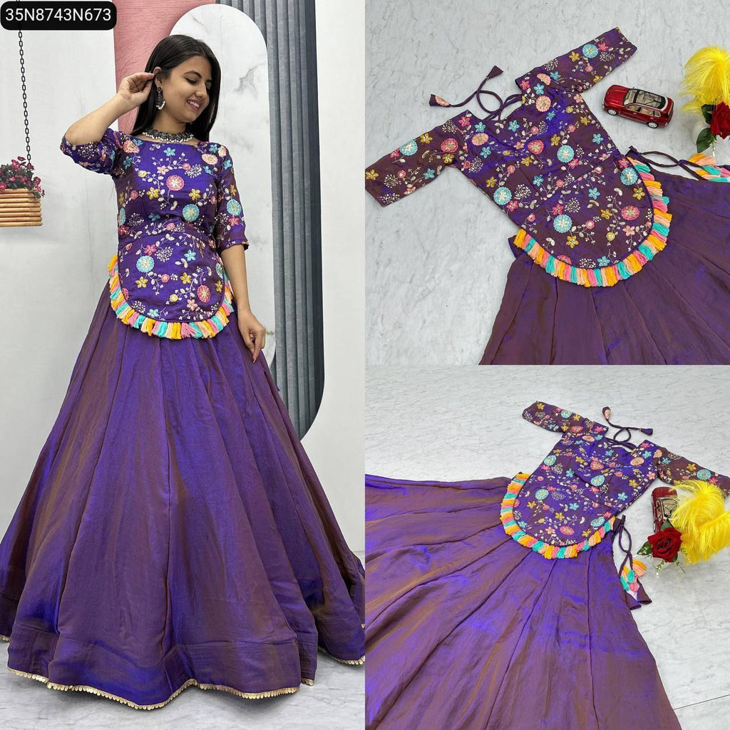 Full body shot of a woman smiling, wearing a vibrant purple lehenga choli set with colorful floral embroidery and tassels.