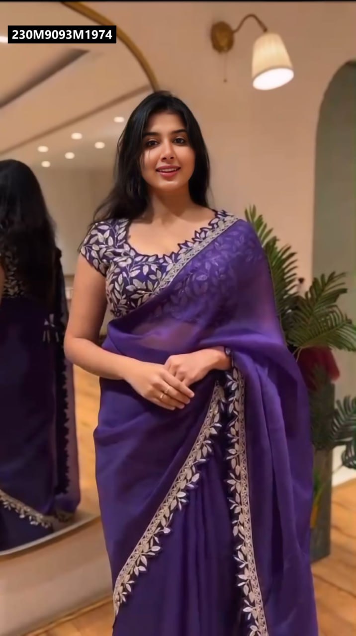 Model posing in a purple Rangoli silk saree with embroidered border and matching blouse, facing front in an indoor setting.