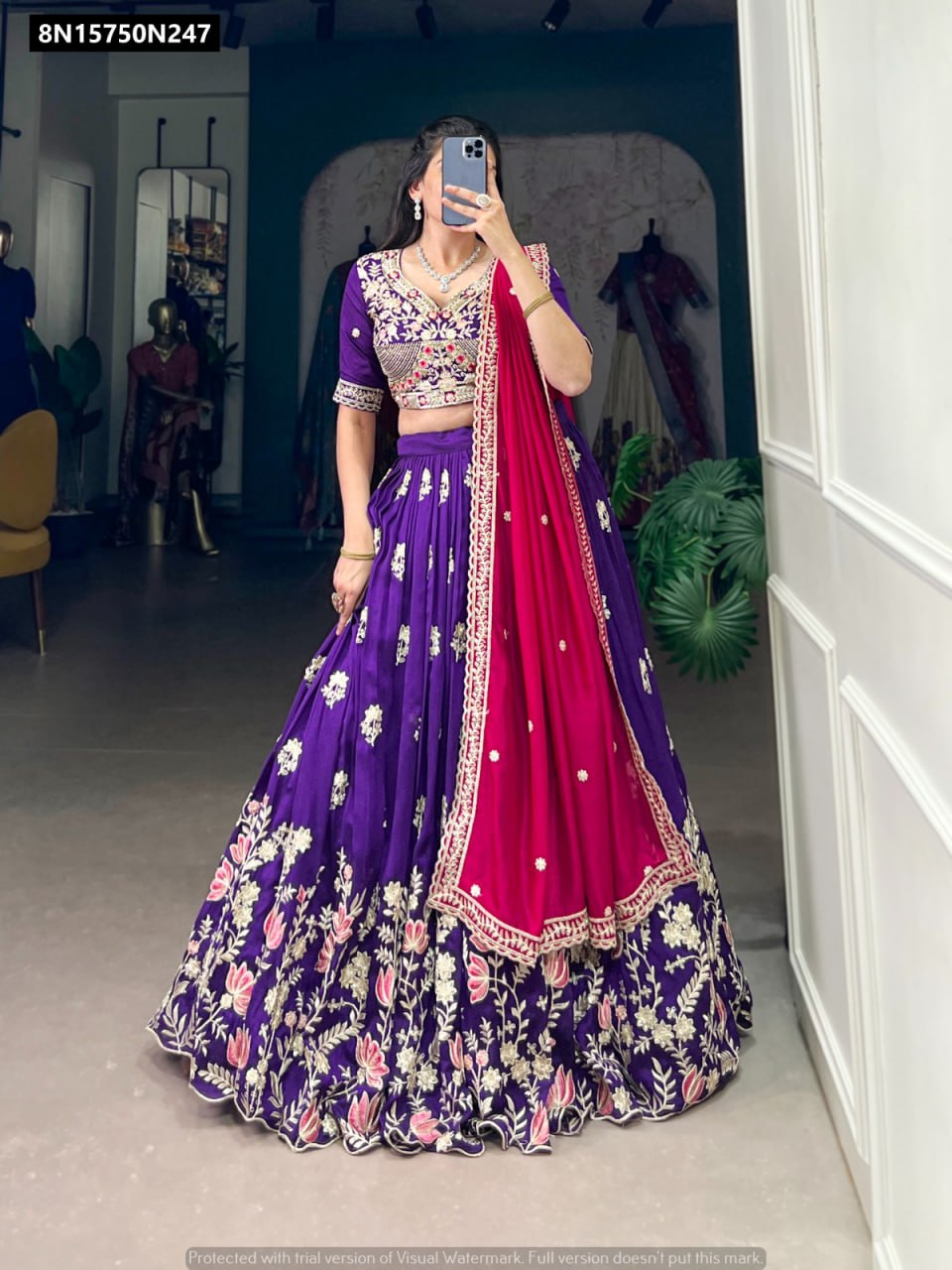 Full-body view of a woman gracefully posing in a TRENDBUY purple Vichitra silk lehenga choli, featuring elaborate floral sequin and thread embroidery on the skirt, paired with a bright pink dupatta, in a well-lit room.