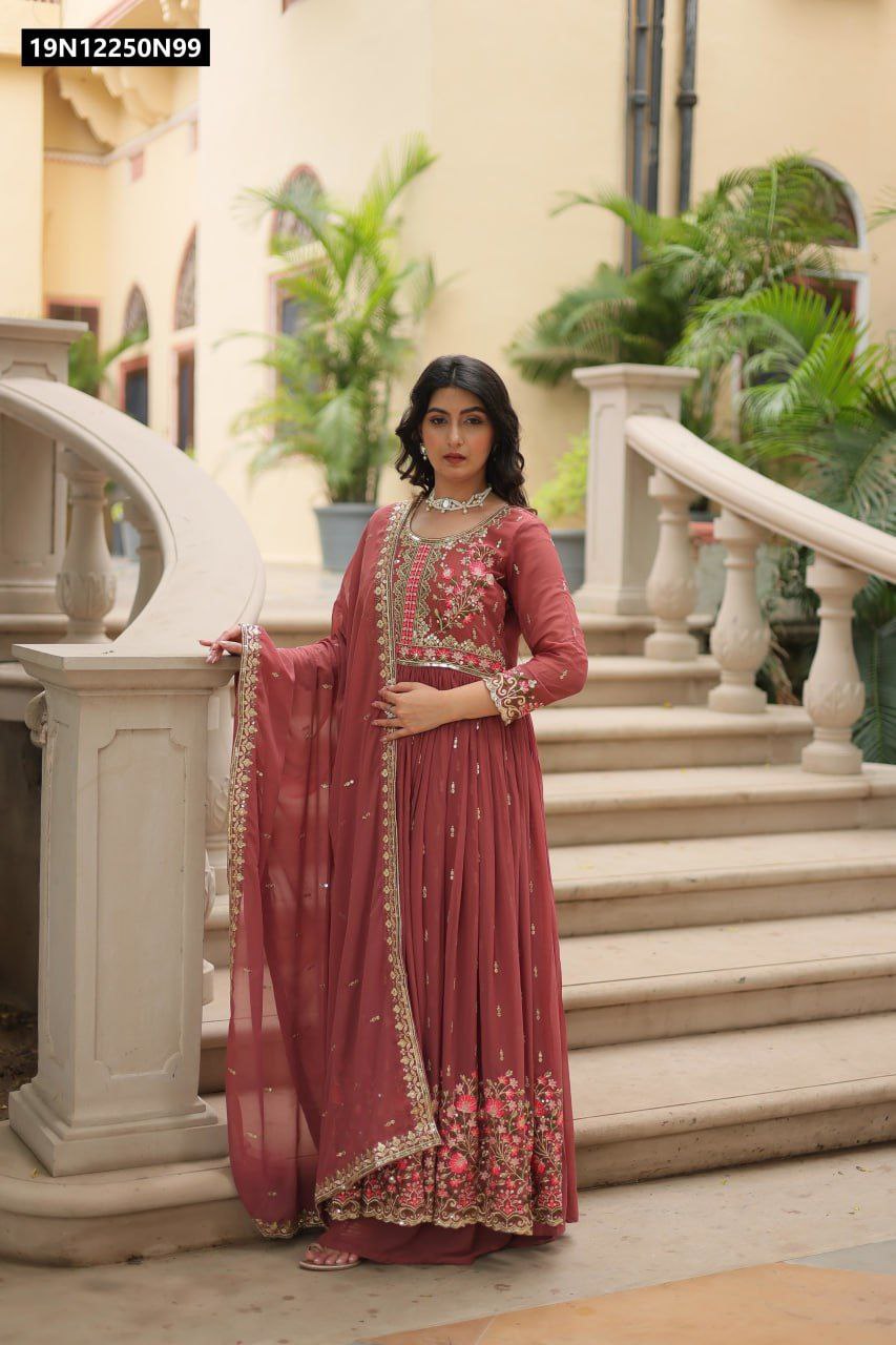 TRENDBUY model posing elegantly in a rust Faux Georgette embroidered Anarkali sharara suit with dupatta on a grand staircase.