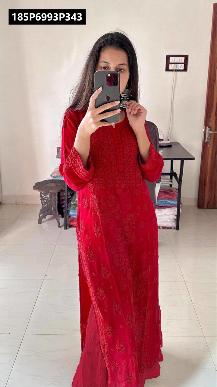 Young woman modeling the TRENDBUY red embroidered Georgette kurta set, standing in a room, holding a smartphone, with long dark hair and silver earrings.