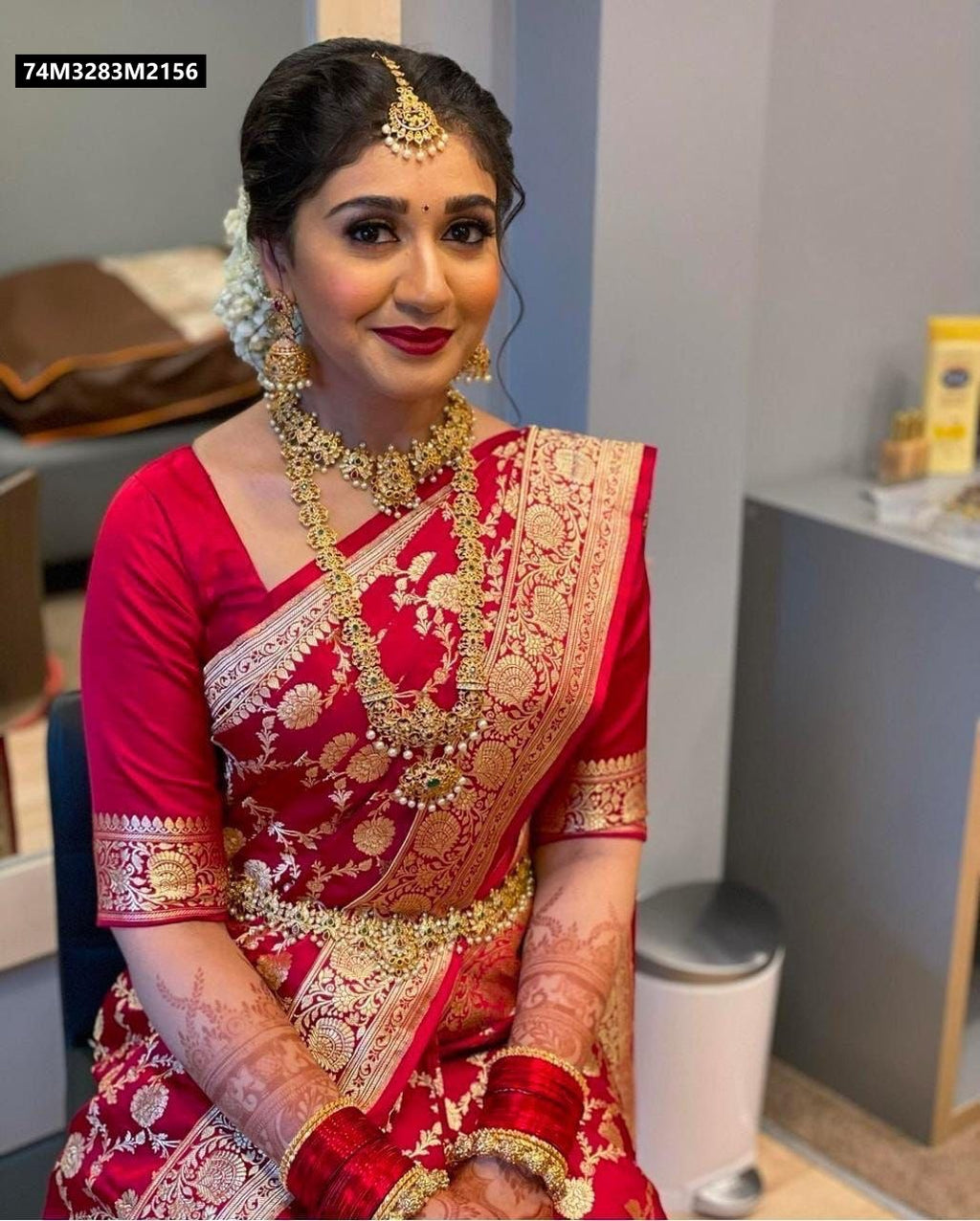 Portrait of a woman elegantly draped in a vibrant red TRENDBUY Lichi Silk saree with intricate gold jacquard work, matching blouse, and traditional gold jewelry, ideal for a wedding.