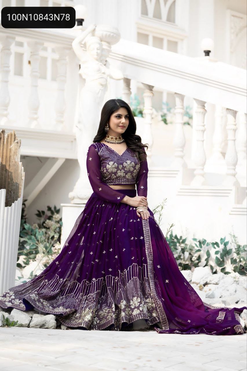 TRENDBUY Regal Purple Fox Georgette Lehenga Choli with intricate gold embroidery and sequence work, worn by a model gracefully seated against a white balustrade.