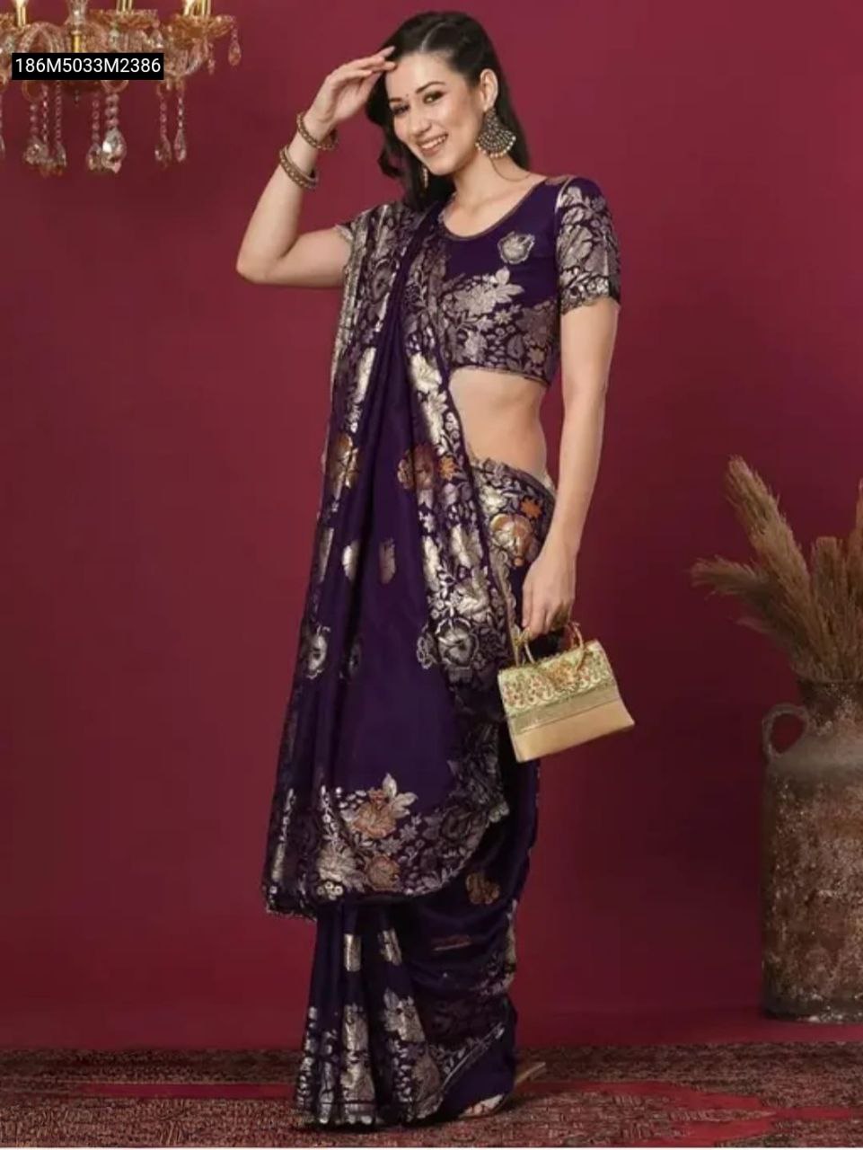 Front view of model in Regal Purple Banarasi soft silk saree with gold zari floral motifs, smiling, holding a gold potli bag.