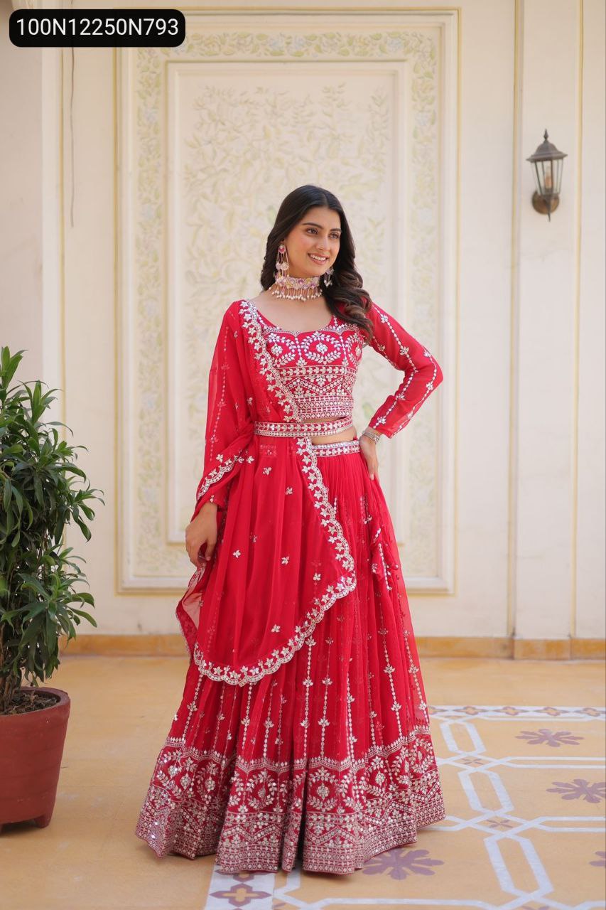 Full body shot of a model posing elegantly in a red sequin embroidered lehenga choli with dupatta draped over her arm, standing outdoors against a decorative wall.