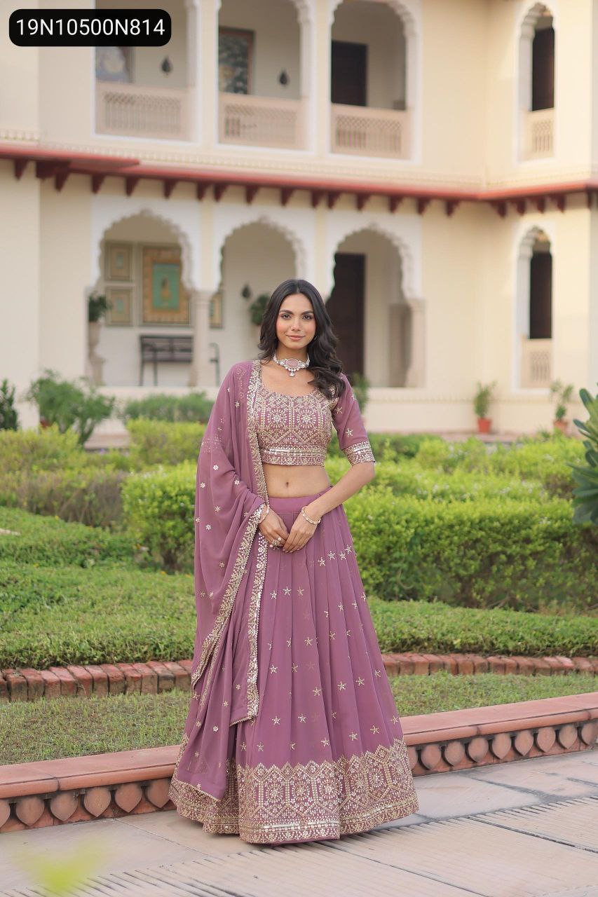 Full body shot of a model wearing a TRENDBUY mauve faux georgette lehenga choli with rich sequin and zari embroidery, posing elegantly in a palace garden.