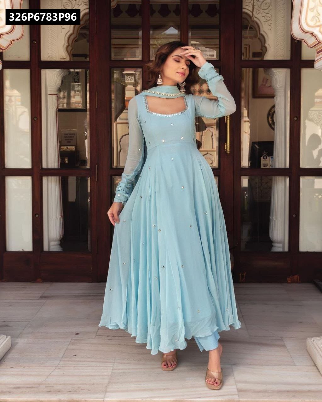 Full body model shot of sky blue Georgette Anarkali with silver handwork, posing confidently in front of a carved wooden door.